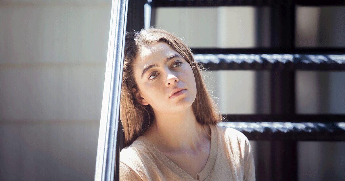Young woman sitting on indoor stairs looking concerned while thinking about the risks of abortion and an unplanned pregnancy